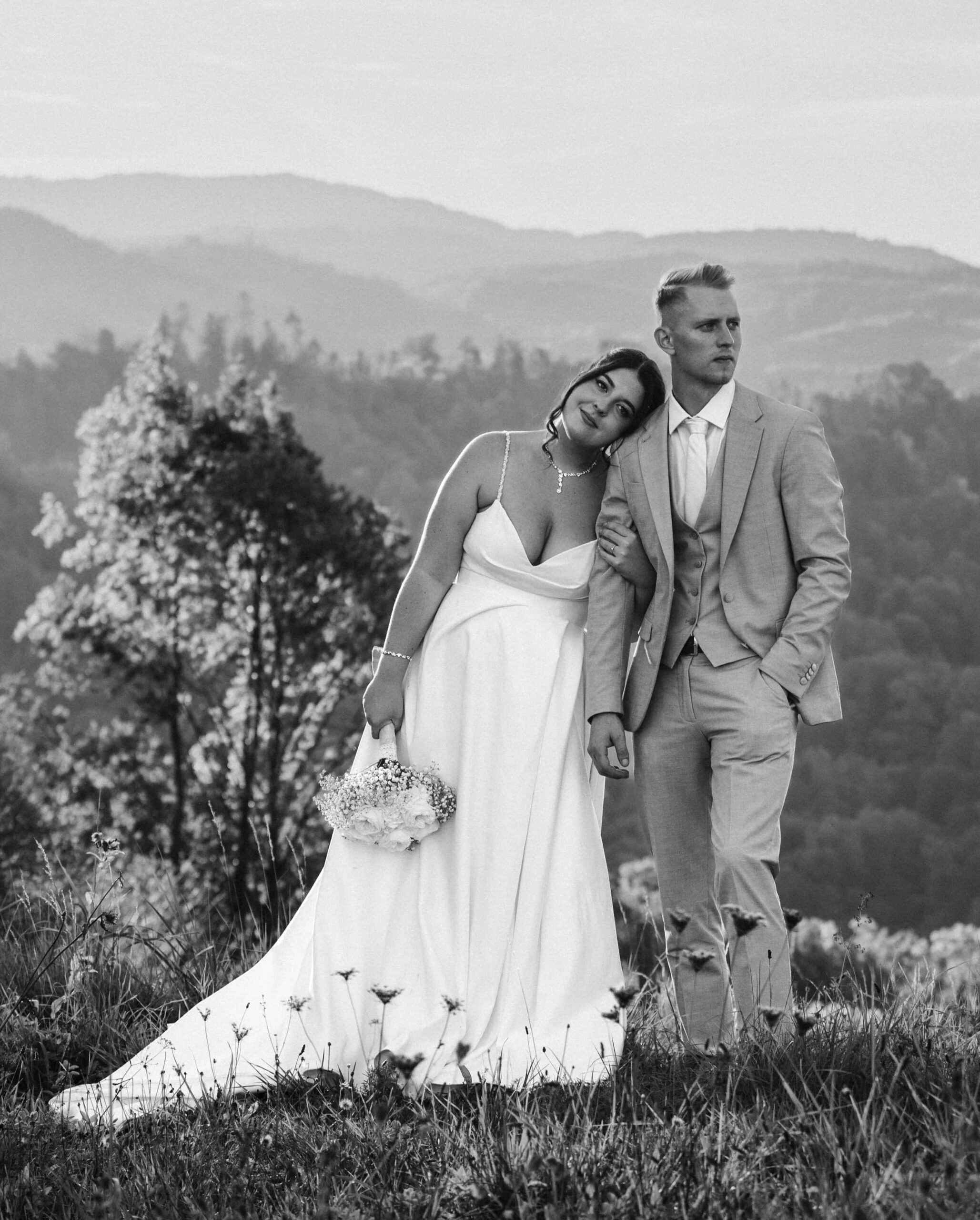 Nevesta in ženin po poroki v Sloveniji, med snemanjem poroke v naravi – sproščen in čuten trenutek ob razgledu na griče.