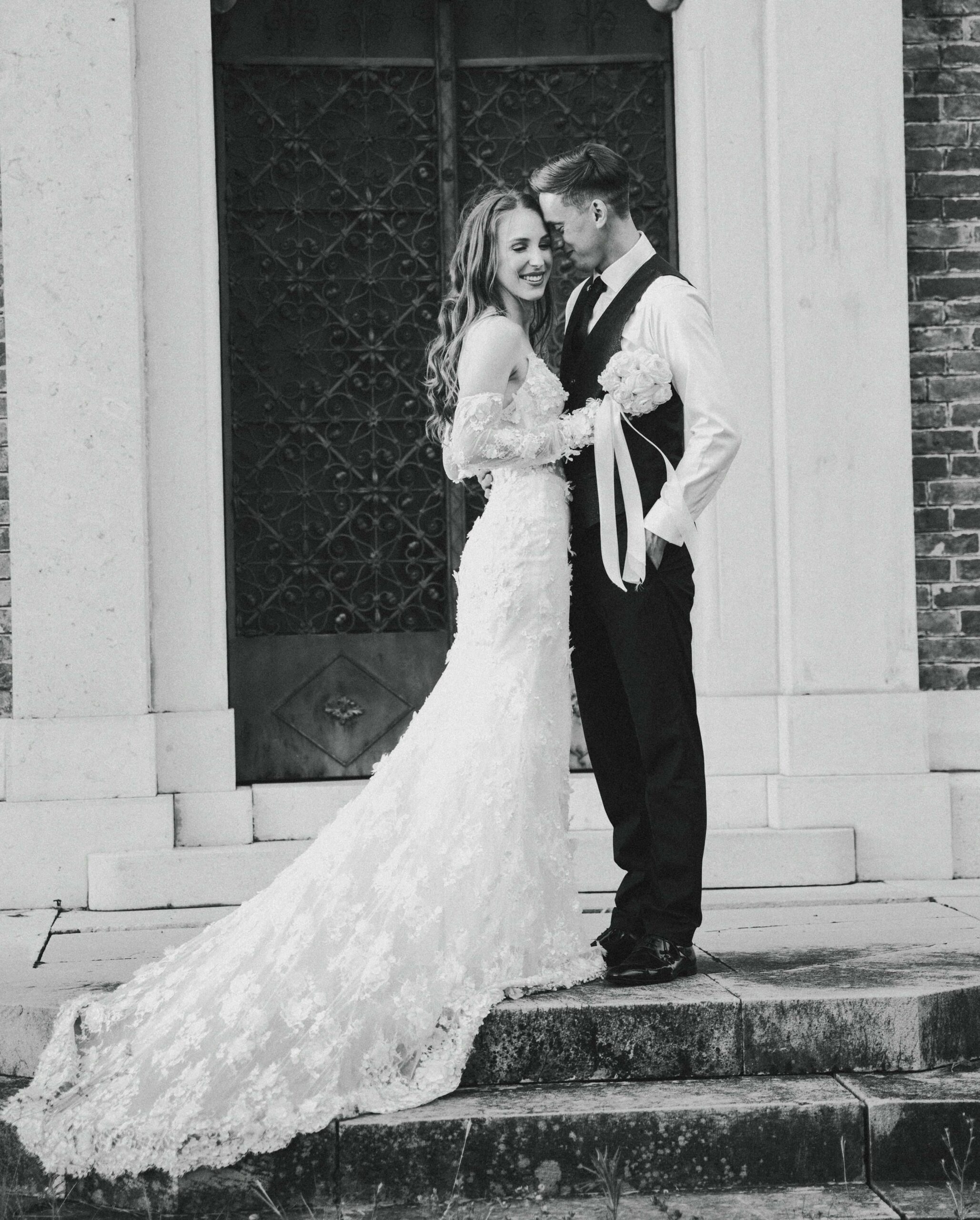 Poročni par pred starinskimi vrati med snemanjem poroke v Sloveniji – eleganten in iskren trenutek ljubezni.